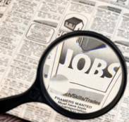 Magnifying glass overlooking a section in the newspaper that shows the word jobs