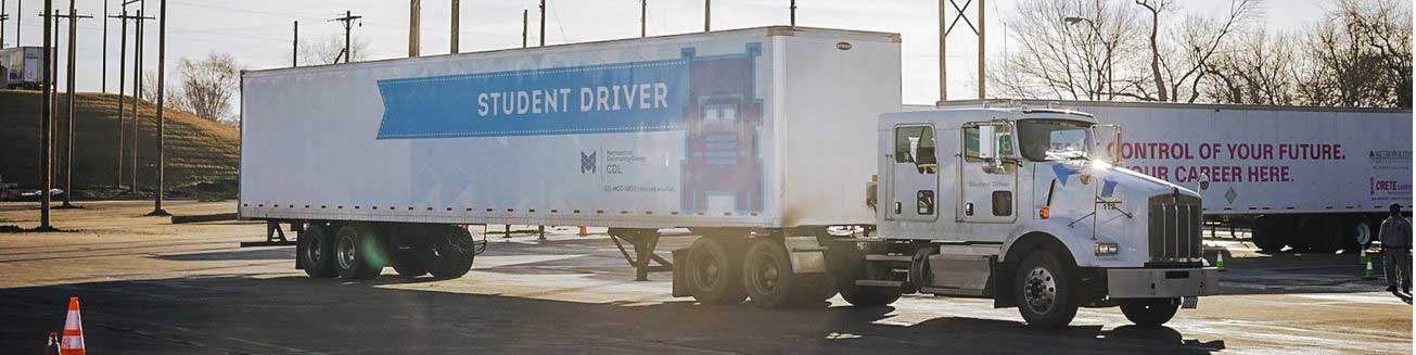 A semi with an MCC CDL-branded trailer that reads "student driver"
